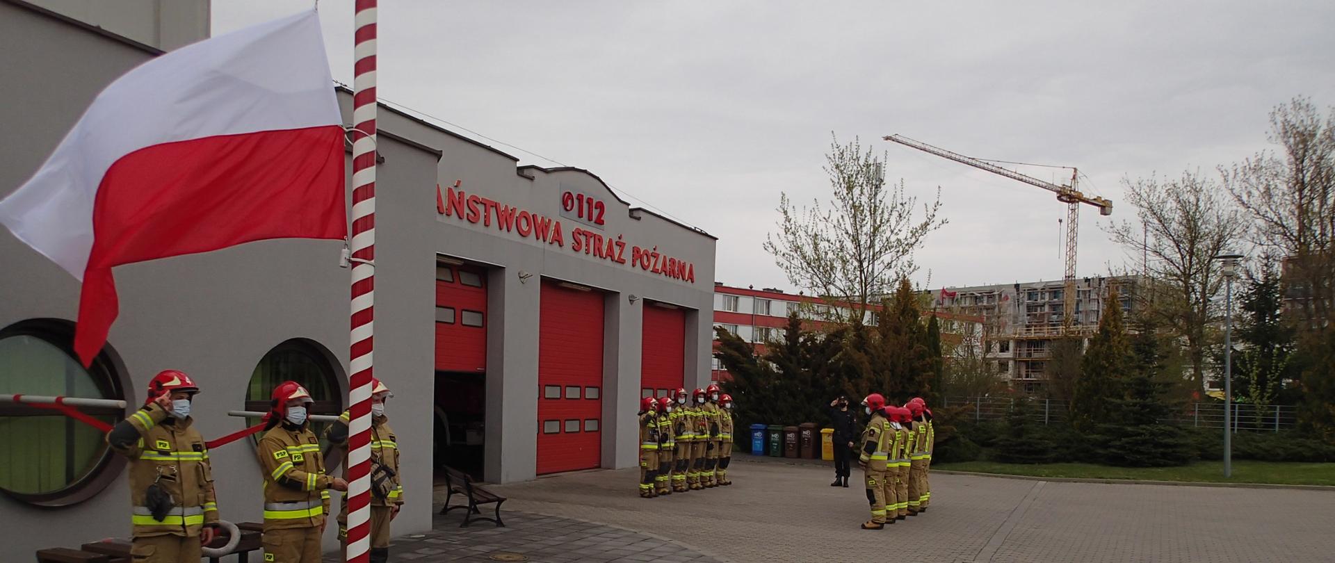 Strażacy wciągają flagę państwową na maszt w tle odgrywany jest Hymn Państwowy. 