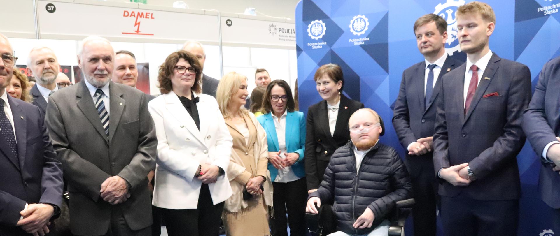 Dyrektor Generalny Ewa Weber stoi wśród innych uczestników Targów Pracy w środku dużej hali. Po prawej stronie ścianka z logotypami Politechniki Śląskiej. 