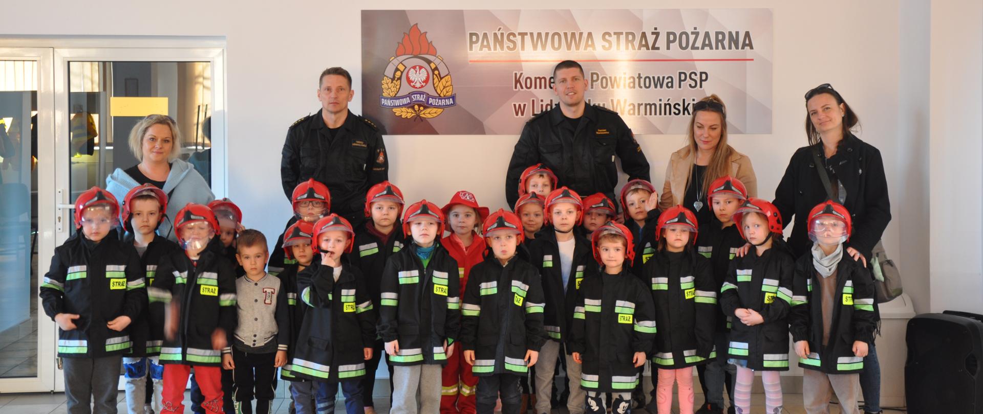 Zdjęcie przedstawia grupę przedszkolną podczas zajęć wraz z Paniami opiekunkami i funkcjonariuszami PSP