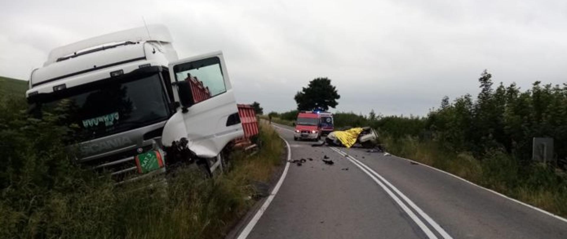 na łuku drogi widać rozbitą ciężarówkę znajdującą się na poboczu oraz kompletnie rozbity pojazd osobowy marki VW GOLF