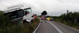 na łuku drogi widać rozbitą ciężarówkę znajdującą się na poboczu oraz kompletnie rozbity pojazd osobowy marki VW GOLF
