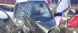 Strażacy prowadzą działania w obrębie wraku pojazdu Toyota Yaris. W tle widać wozy pożarnicze oraz karetkę PRM. 