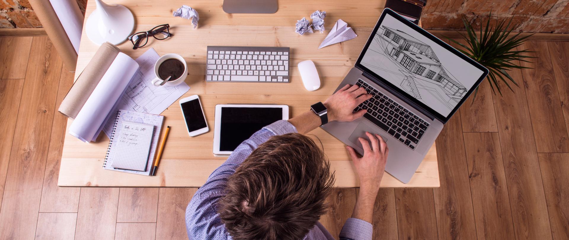 Architekt przy biurku. Projektuje z użyciem laptopa.