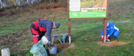 Dwaj mężczyźni wkopujący tablicę informacyjną w otwory w ziemi. 