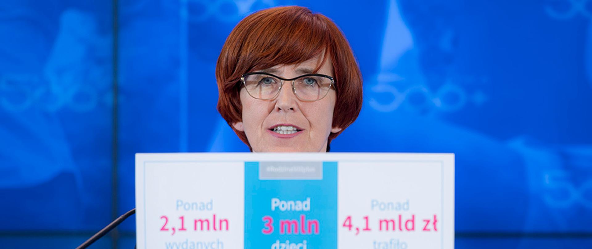 Konferencja podsumowującej trzy miesiące działania programu rodzina 500+. Minister Rafalska trzyma kartę z liczbą złożonych wniosków 500+, wydanymi środkami oraz liczbą dzieci otrzymujących świadczenia.