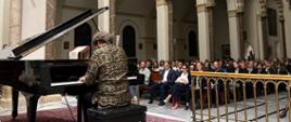 A man plays the piano in a church, with the audience listening in the background