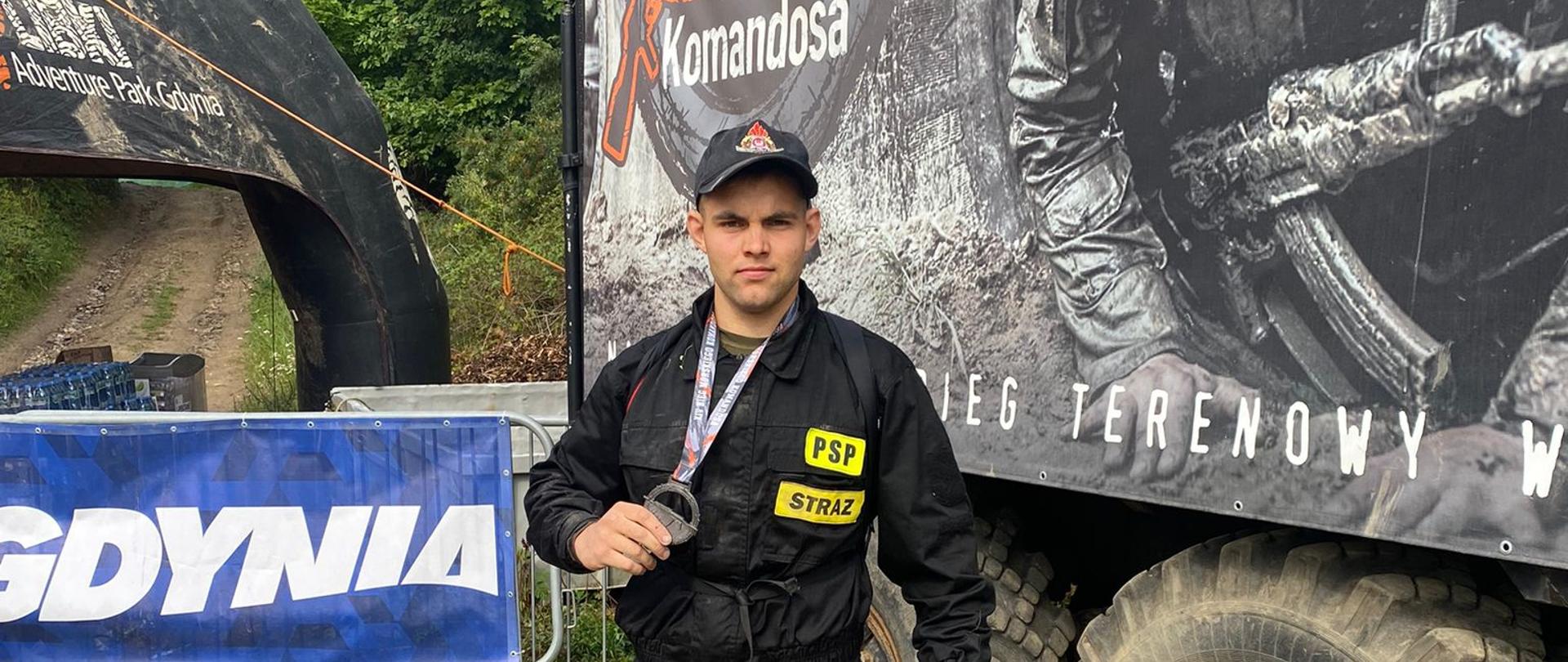 Zdjęcie przedstawia strażaka na tle wozu wpjskowego w ręku trzymającego medal.