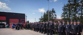 Grupa strażaków stojąca w dwuszeregu, w oddali sztandary