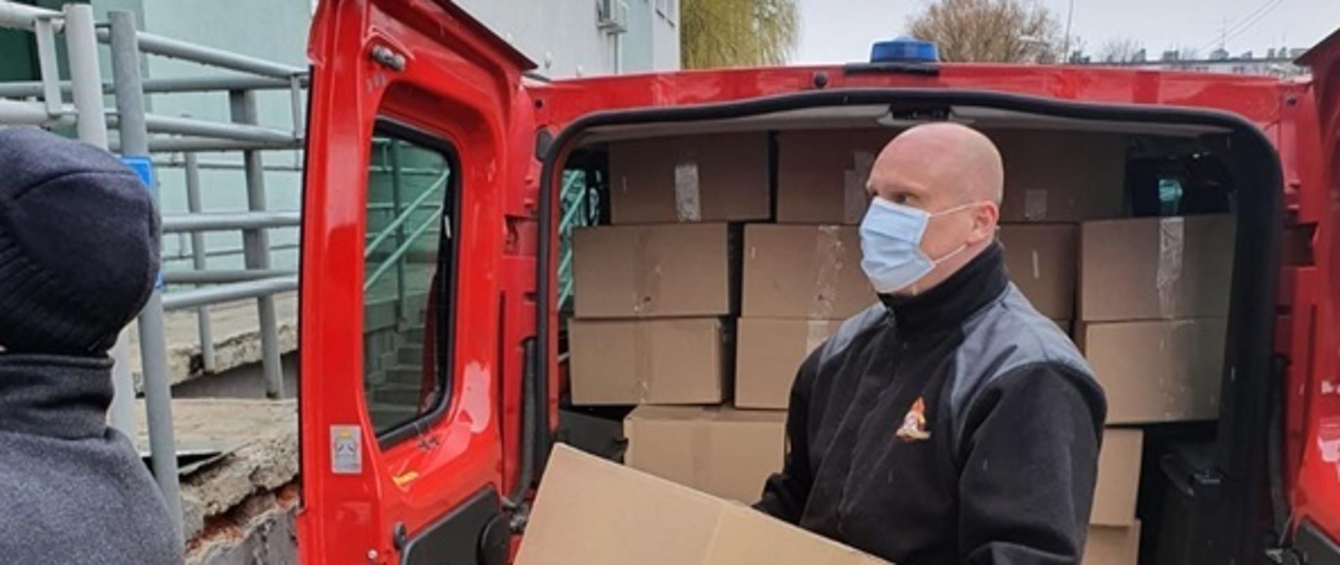 Zdjęcie przedstawia strażaka w trakcie dystrybucji maseczek do punktów szczepień