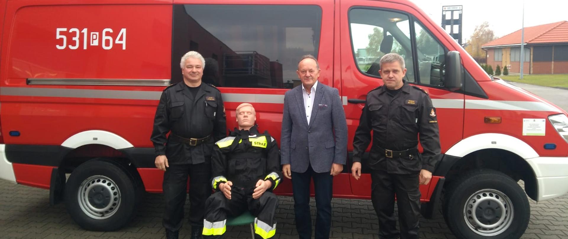Komendanci, sponsor oraz manekin na tle samochodu pożarniczego.