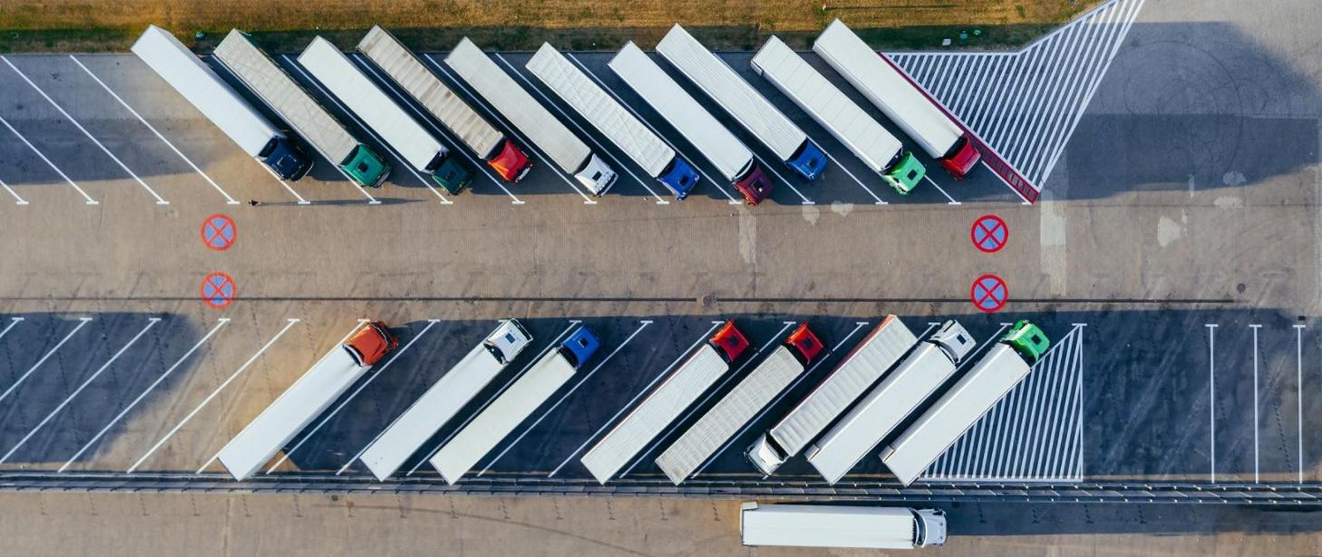 Kilkanaście pojazdów ciężarowych stoi na parkingu. Widok z góry.