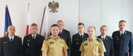 Na tle flag oraz godła stoi kilku strażaków w mundurach.