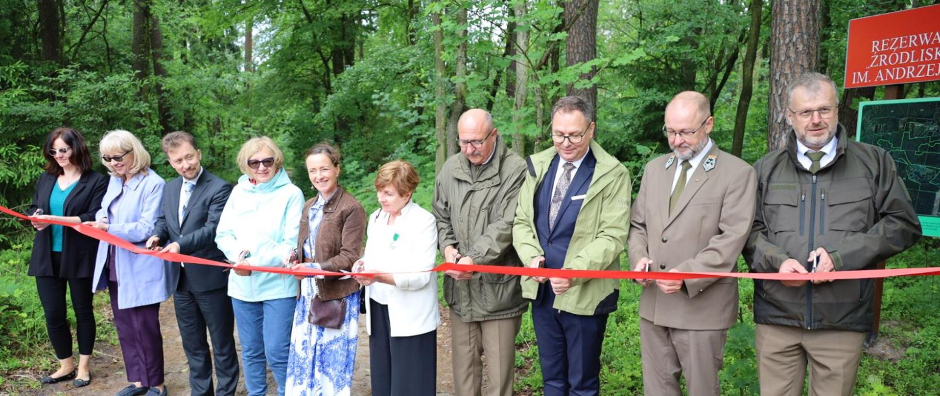 Grupa ludzi w lesie przecina czerwoną wstęgę