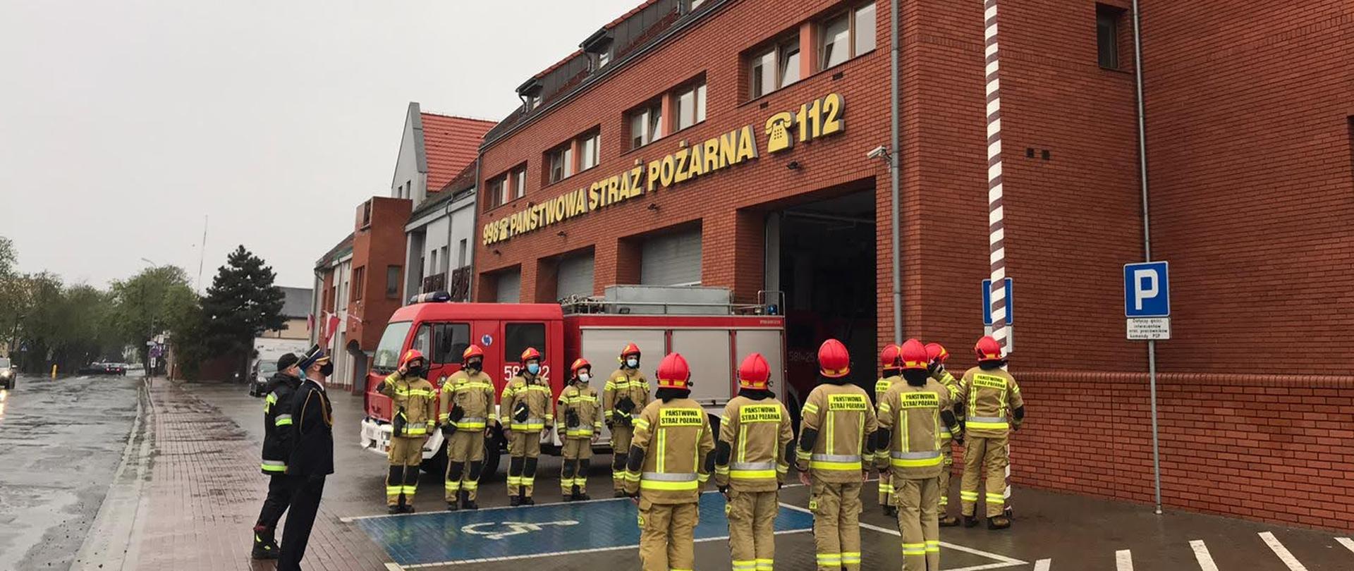 Strażacy stoją przy maszcie gzie jest podnoszona flaga