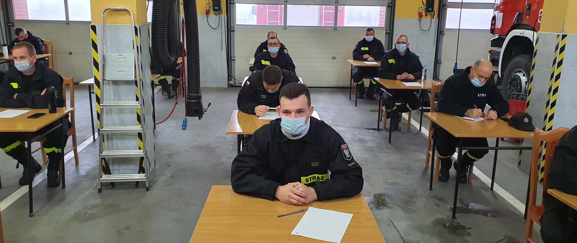 Na zdjęciu druhowie OSP siedzą przy stolikach i piszą egzamin dowódców OSP