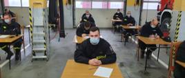 Na zdjęciu druhowie OSP siedzą przy stolikach i piszą egzamin dowódców OSP