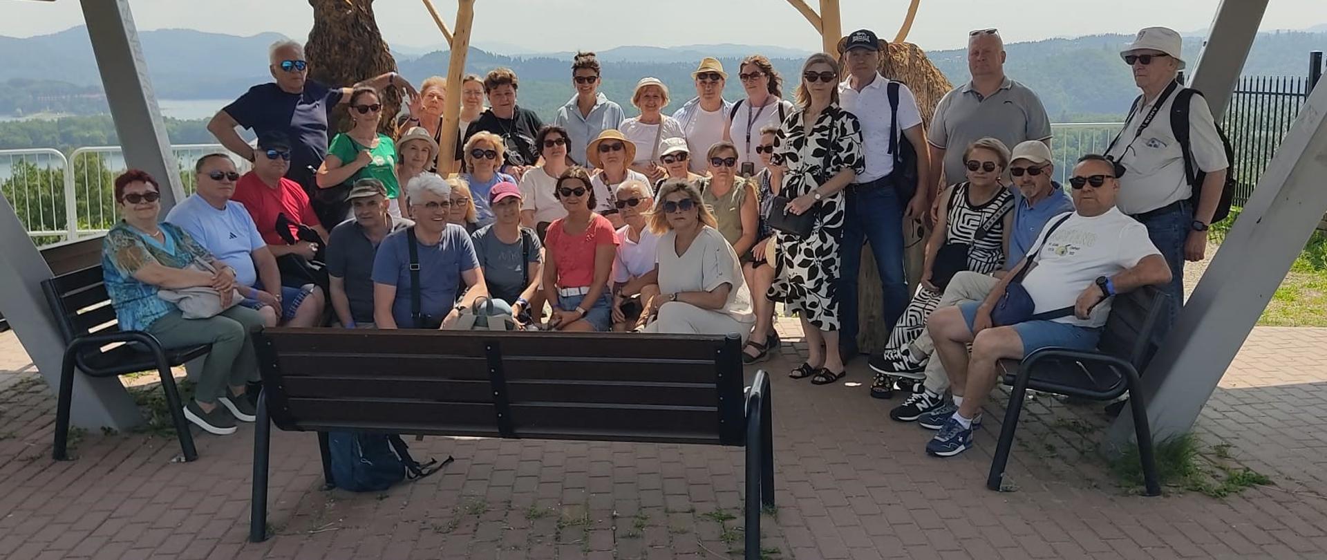 Na zdjęciu grupa kilkudziesięciu członków ZEiRP RP. Siedzą na ławkach pod spadzistym zadaszeniem. W tle górzysty teren.