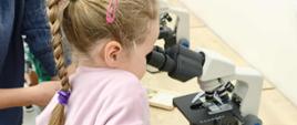 Dziewczynka obserwuje preparat pod mikroskopem.
