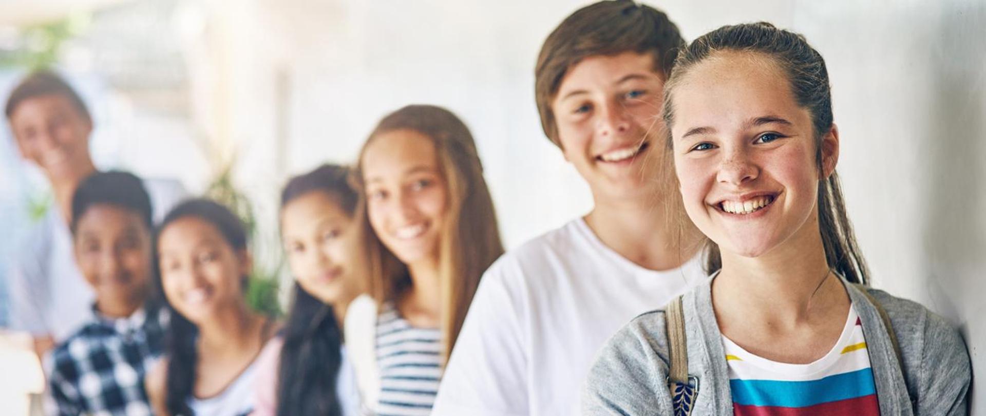  Uśmiechnięci uczniowie zebrani przed białą tablicą, prowadzący dyskusję na temat lekcji.