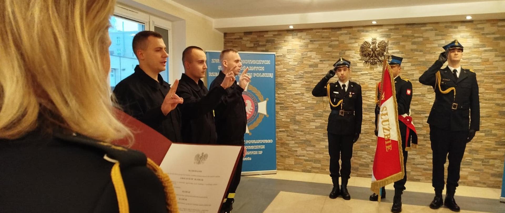 Na zdjęciu 3 funkcjonariuszy po lewej stronie podczas ślubowania, obok stoi poczet sztandarowy ze sztandarem