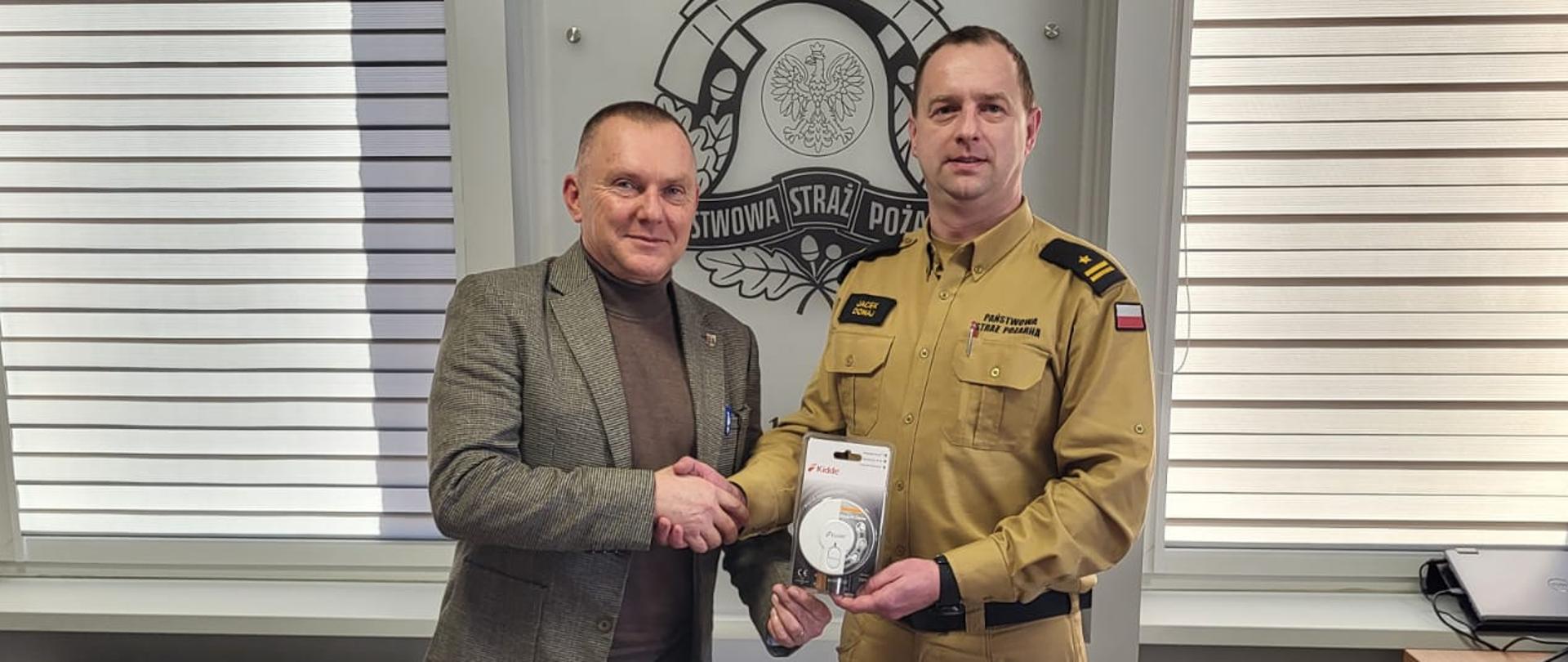  Na zdjęciu Starosta Kościański wręcza symbolicznie czujkę dymu na ręce Komendanta Powiatowego PSP w Kościanie.