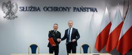 Na zdjęciu widać jak Komendant Główny PSP gen. brygadier Andrzej Bartkowiak podaje dłoń komendantowi Służby Ochrony Państwa po podpisaniu porozumienia. W tle flagi Polski