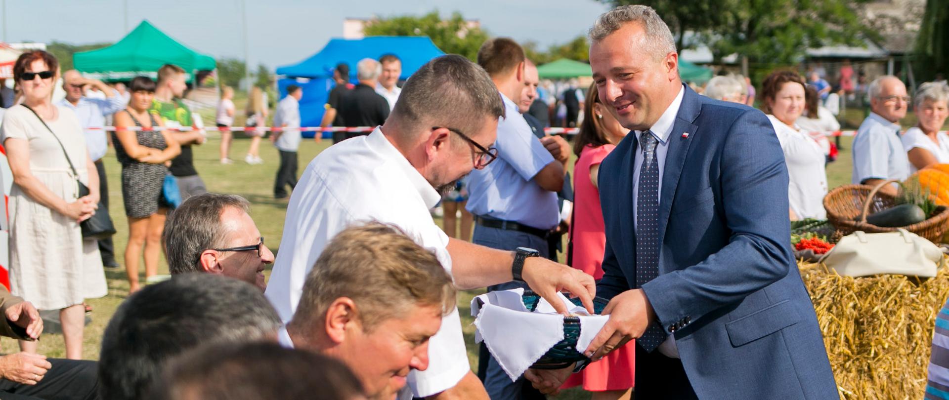 wojewoda Mikołaj Bogdanowicz na pikniku na trawie rozdaje chleb z kosza, wokół tłum ludzi 