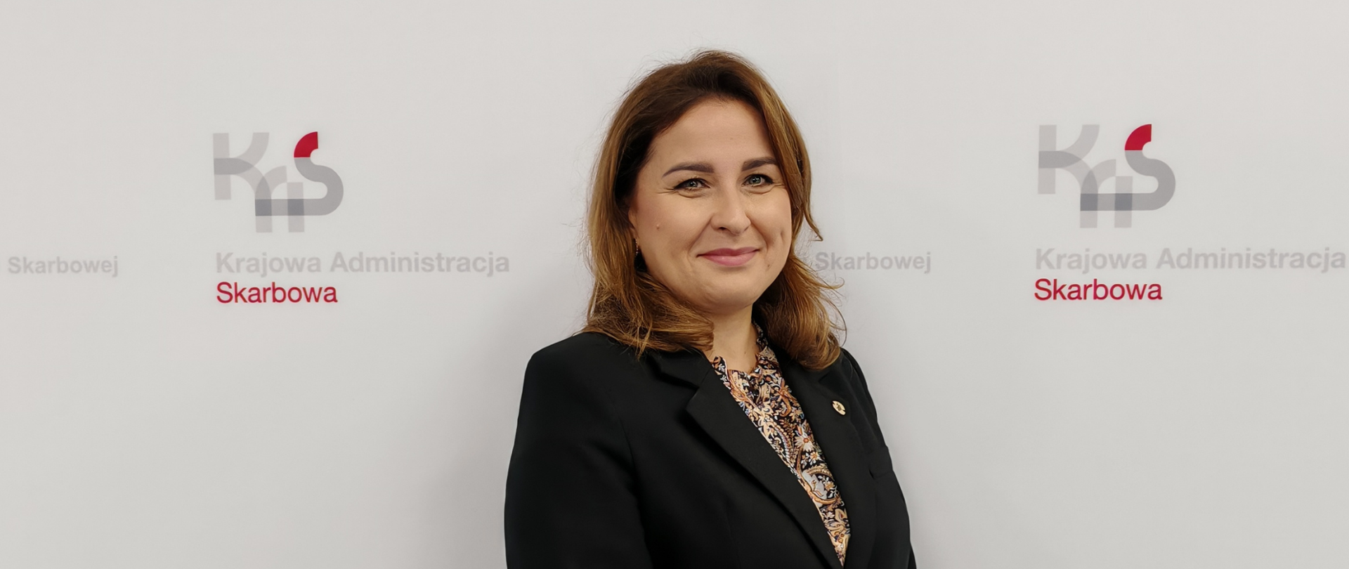 Kobieta na tle ściany z logo KAS i napisami Izba Administracji Skarbowej w Bydgoszczy