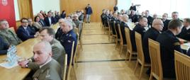 Uczestnicy narady rocznej Kadry Kierowniczej Państwowej Straży Pożarnej województwa opolskiego. Na zdjęciu widać, jak wszyscy uczestnicy siedzą przy dwóch stołach, po lewej oraz po prawej stronie zdjęcia. 