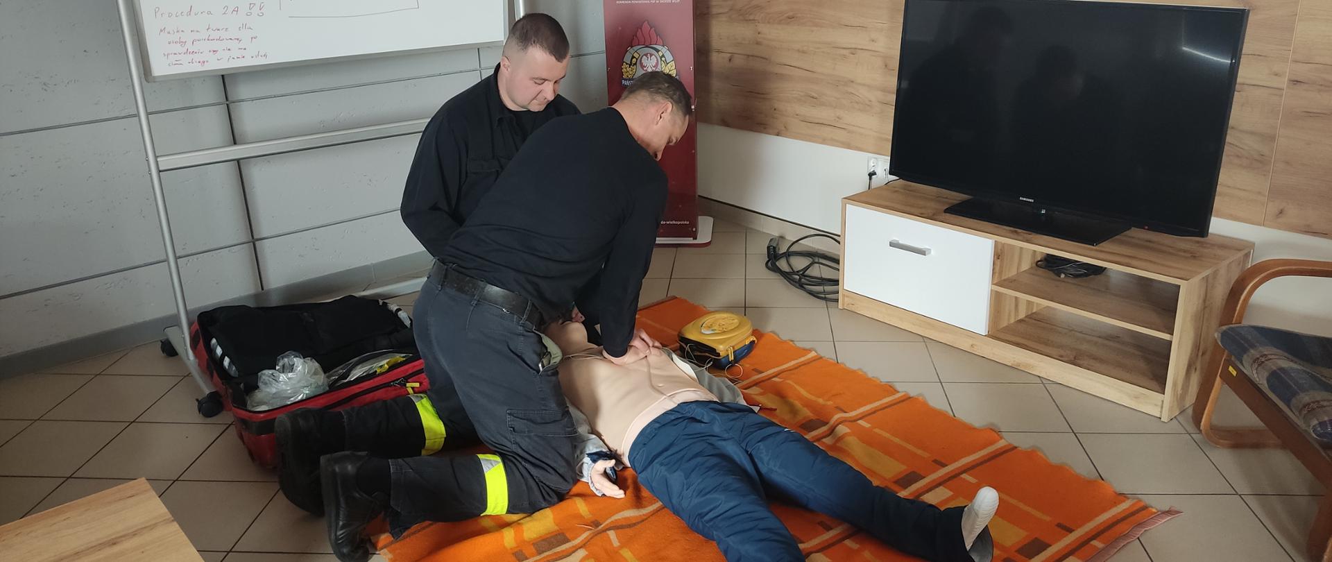 Strażacy na świetlicy podczas doskonalenia zawodowego z zakresu KPP z wykorzystaniem fantoma osoby dorosłej wykonujący uciski klatki piersiowej