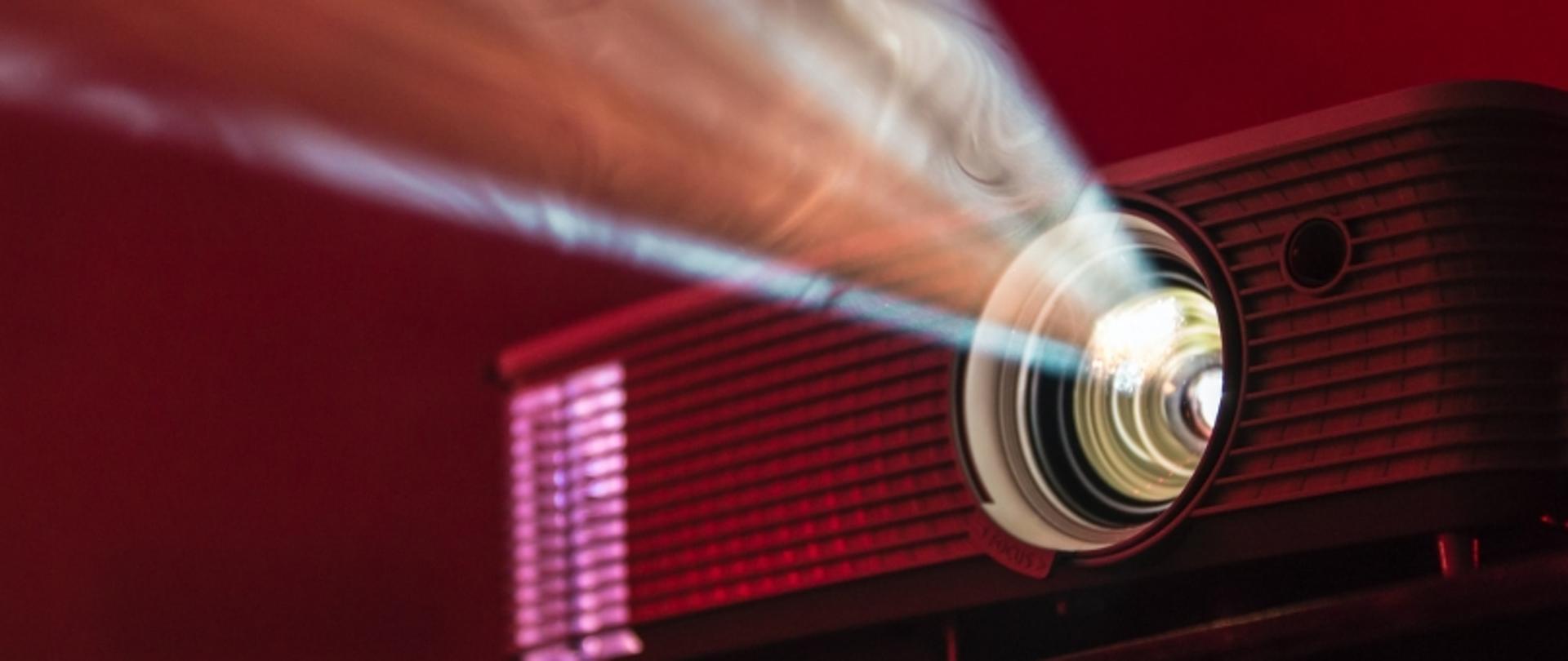 Zbliżenie na działający projektor emitujący światło w ciemnym, czerwono oświetlonym pomieszczeniu.