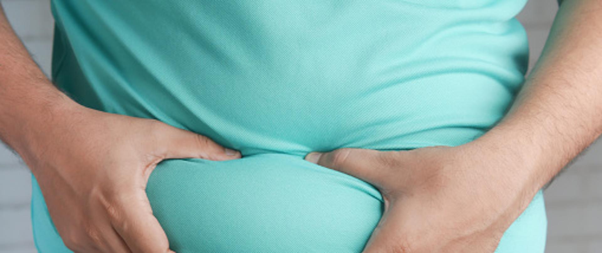 man's hand holding excessive belly fat, overweight concept.