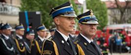 Widok z boku. Na pierwszym planie zastępca małopolskiego komendanta wojewódzkiego PSP, na drugim planie komendant powiatowy PSP. W tle strażacy.