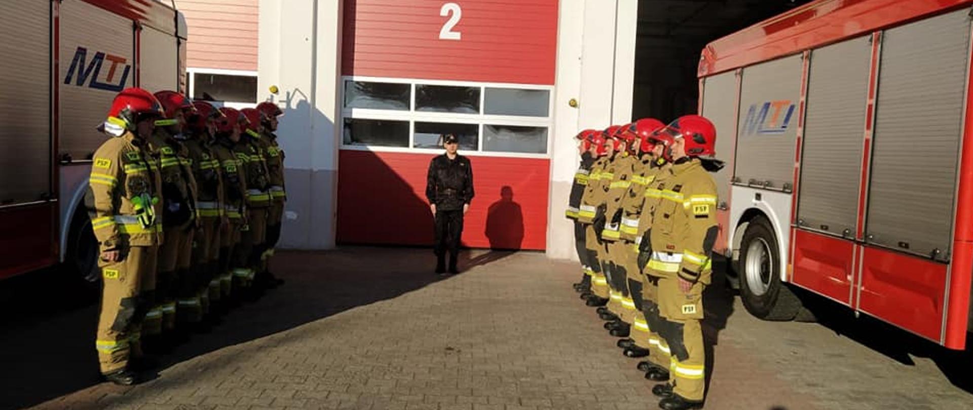 Zmiana służbowa w obecności dowódcy JRG poświęcona uczczeniu minutą ciszy pamięci poległych ukraińskich strażaków. Strażacy w umundurowaniu specjalnym stoją na baczność w dwóch rzędach naprzeciwko siebie.