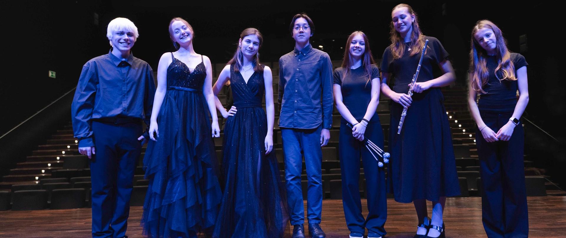 Zdjęcie przedstawia uczestników koncertu we wspólnym zdjęciu na scenie sali koncertowej filharmonii