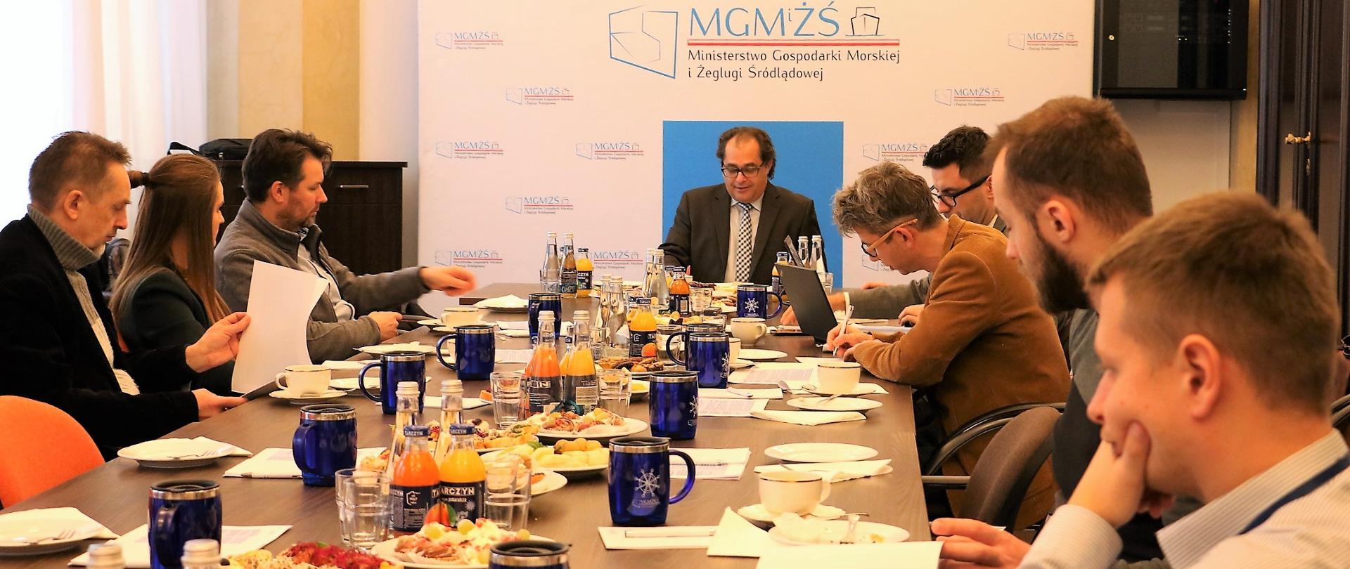 Uczestnicy spotkania siedzą przy wspólnym stole. Spotkaniu przewodniczy minister M. Gróbarczyk