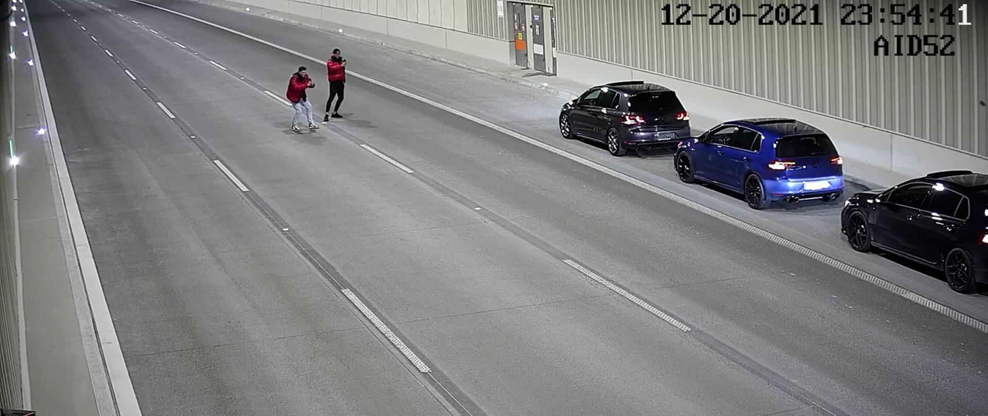 Przykład nieodpowiedzialnych zachowań użytkowników tunelu na S2POW pod Ursynowem. Trzy zaparkowane na pasie awaryjnym pojazdy po prawej stronie fotografii oraz dwóch mężczyzn na środku tunelu robiących zdjęcia tych pojazdów.