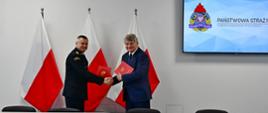 Pomorski komendant wojewódzki Państwowej Straży Pożarnej trzyma dłoń wójta gminy Kobylnica. Oboje trzymają czerwone teczki.