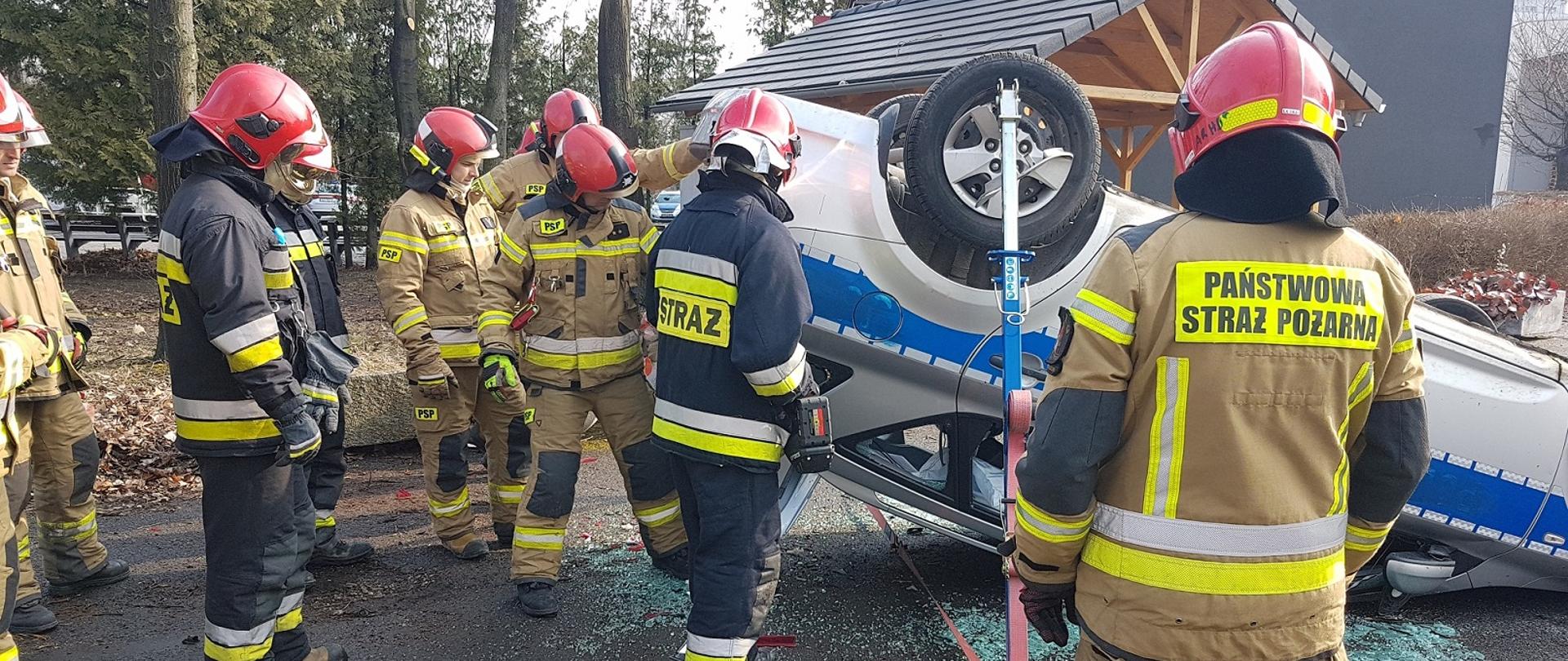 Strażacy PSP podczas szkolenia z ratownictwa technicznego na poziomie podstawowym. Strażacy w umundurowaniu specjalnym wykonali stabilizację pojazdu leżącego na dachu. 