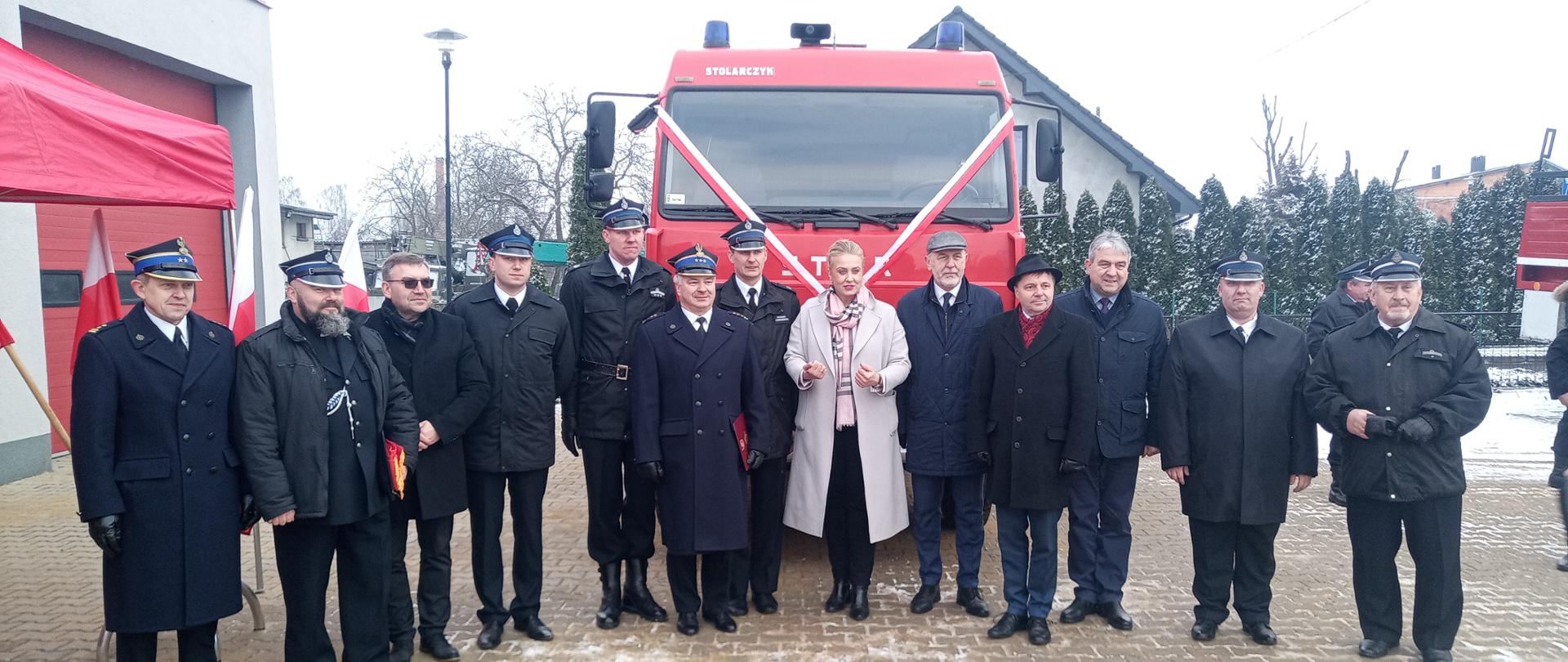 Funkcjonariusze PSP, druhowie OSP przedstawiciele gminy, posłowie oraz zaproszeni goście w tle samochód strażacki