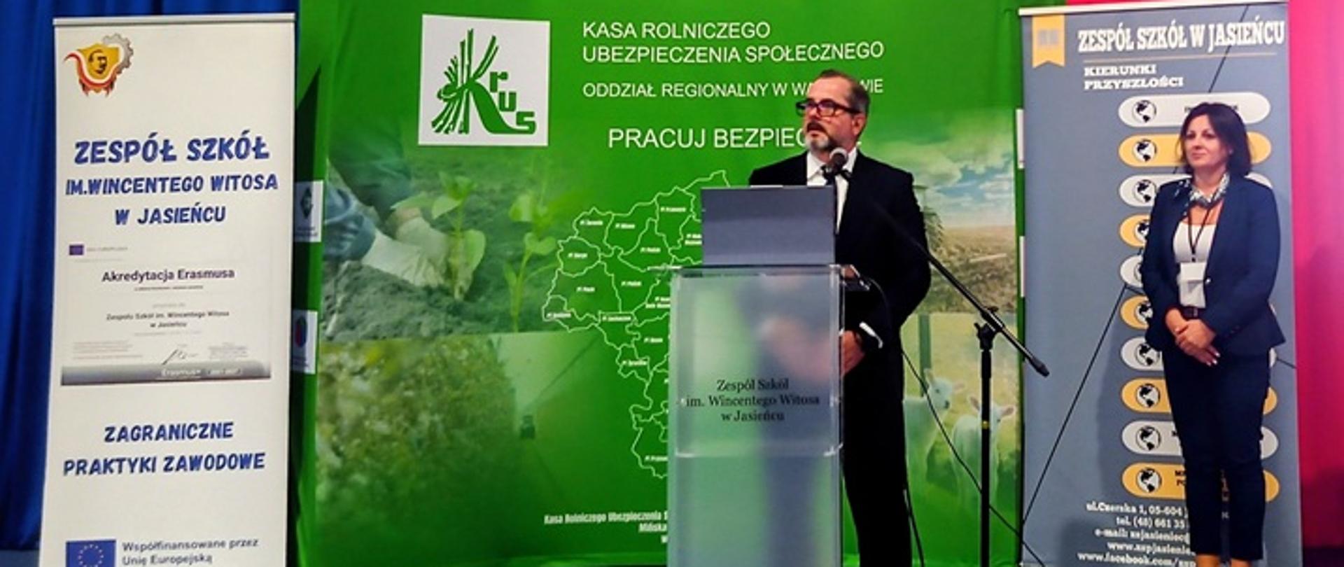 Przemawiający na tle baneru z mapą Polski