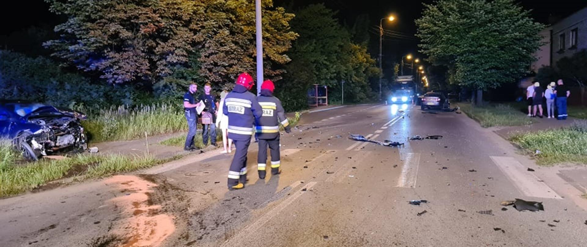Na zdjęciu widzimy kolizję dwóch samochodów osobowych VW Passat oraz Ford Focus na skrzyżowaniu ul. Pięknej z ul. 1-go Maja w Skarżysku-Kamiennej. Na pierwszym planie po lewej stronie zdjęcia widzimy znajdujący się na poboczu samochód osobowy Ford Focus, w dalszym planie po prawej stronie zdjęcia widzimy znajdujący się na drodze samochód VW Passat. Samochód Ford Focus w wyniku zdarzenia ma całkowicie rozbity przód pojazdu. Z pojazdu na chodnik i ulicę wyciekły płynny eksploatacyjne, które strażacy posypali sorbentem Compact. Na ulicy widzimy porozrzucane elementy karoserii obu uszkodzonych pojazdów.