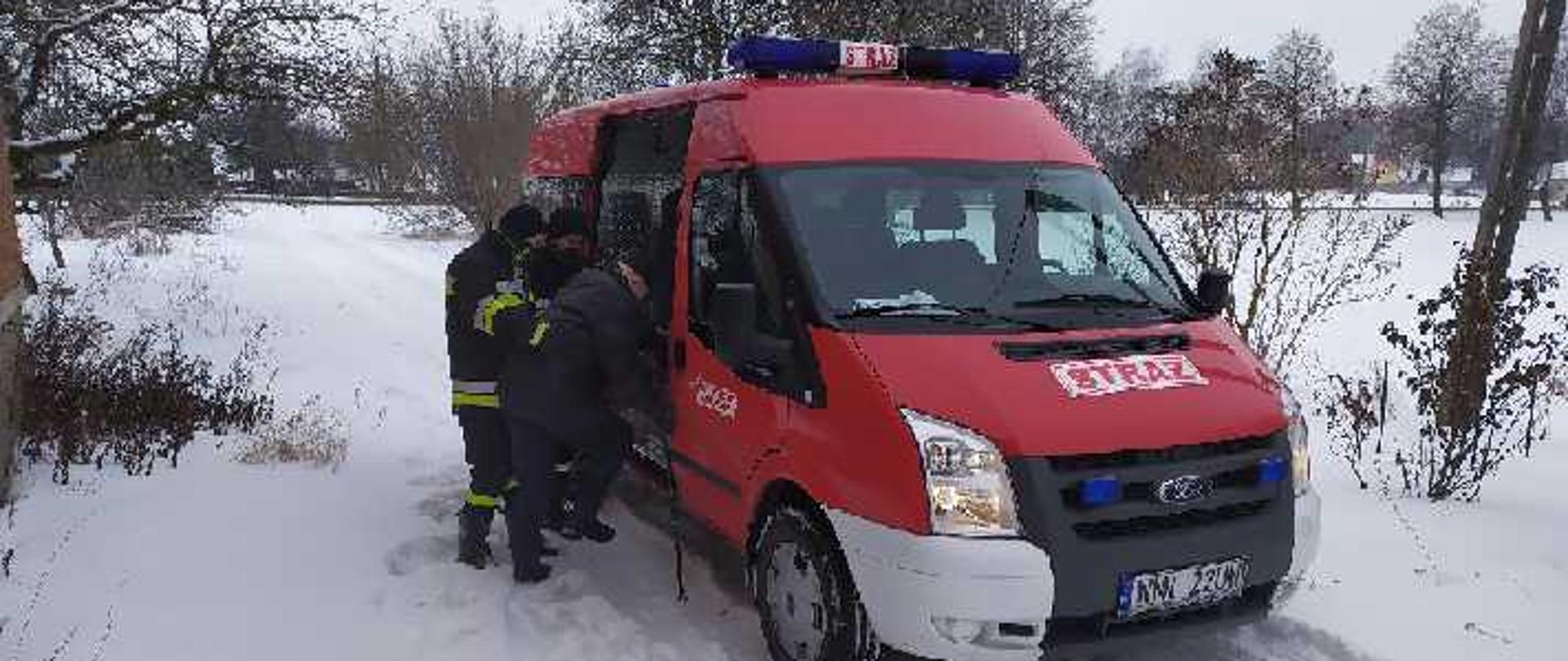 Na zdjęciu widać strażaka pomagającego wsiąść do samochodu straży pożarnej. zimowa aura.