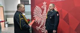 Komendant wręcza szczęśliwemu emerytowi decyzje.