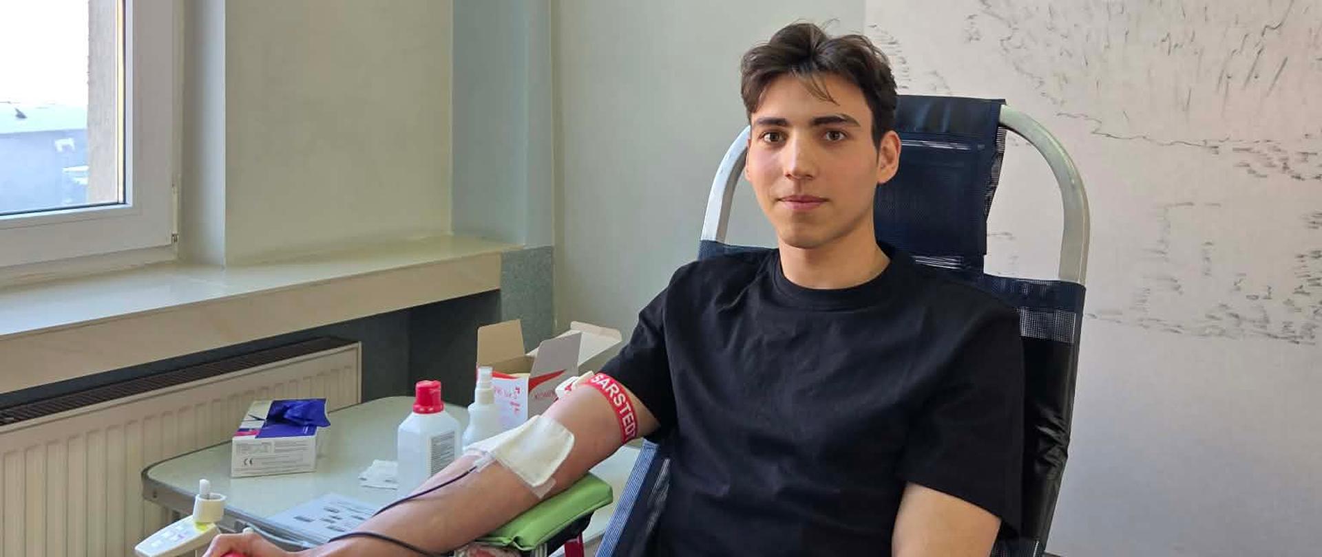 Uczeń ubrany na czarno, siedzący na fotelu w trakcie oddawania krwi.