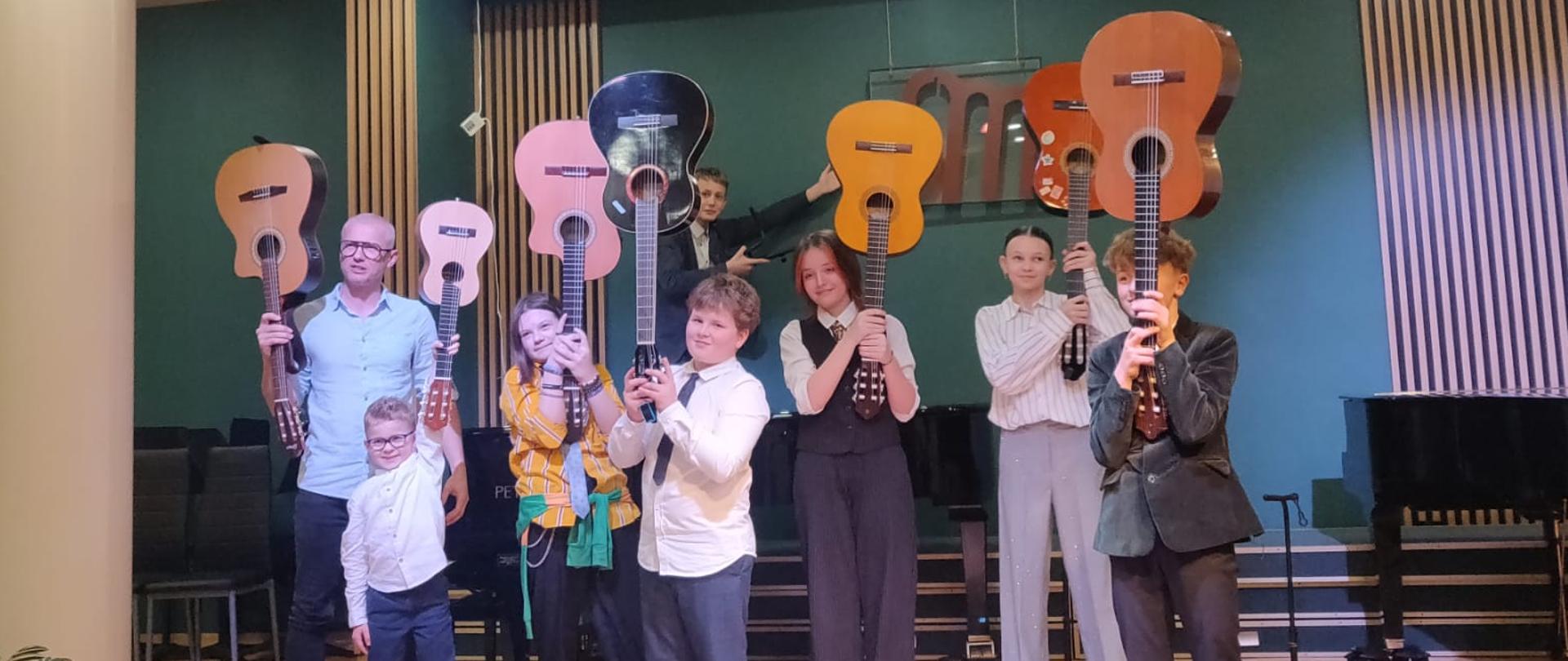 Uczniowie klasy gitary trzymają w rękach gitary skierowane do sufitu.