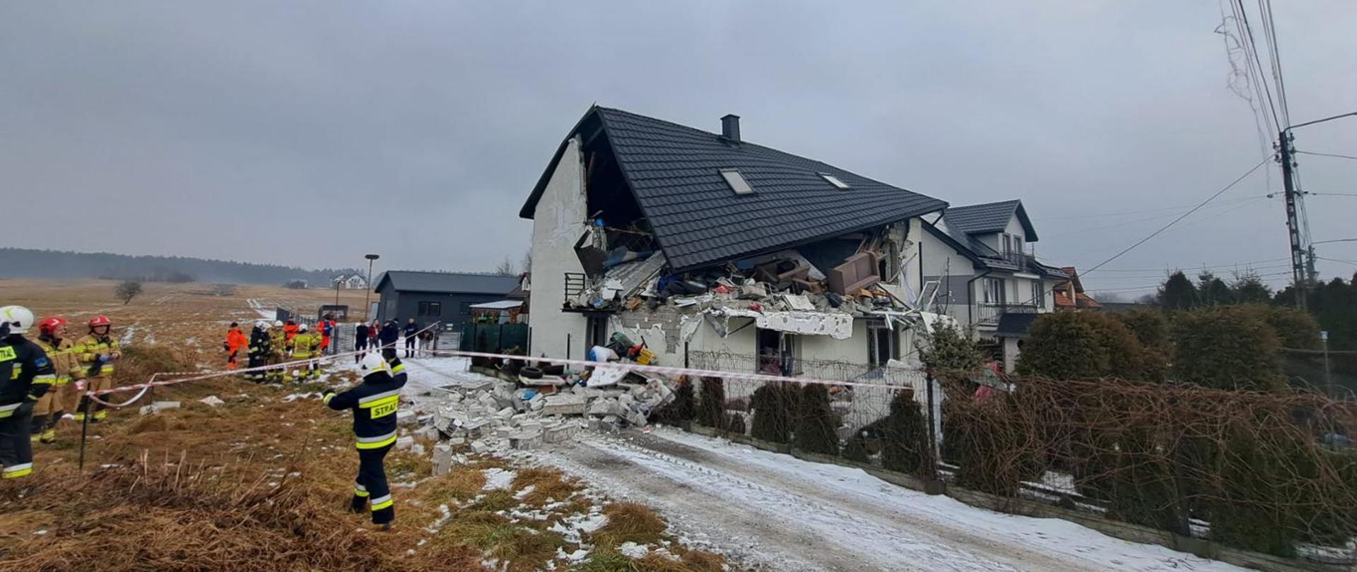 Wybuch w Brzezinkach - na zdjęciu widoczne zniszczenia domu, sstrażacy odgradzają teren taśmą. Pochmurna aura.