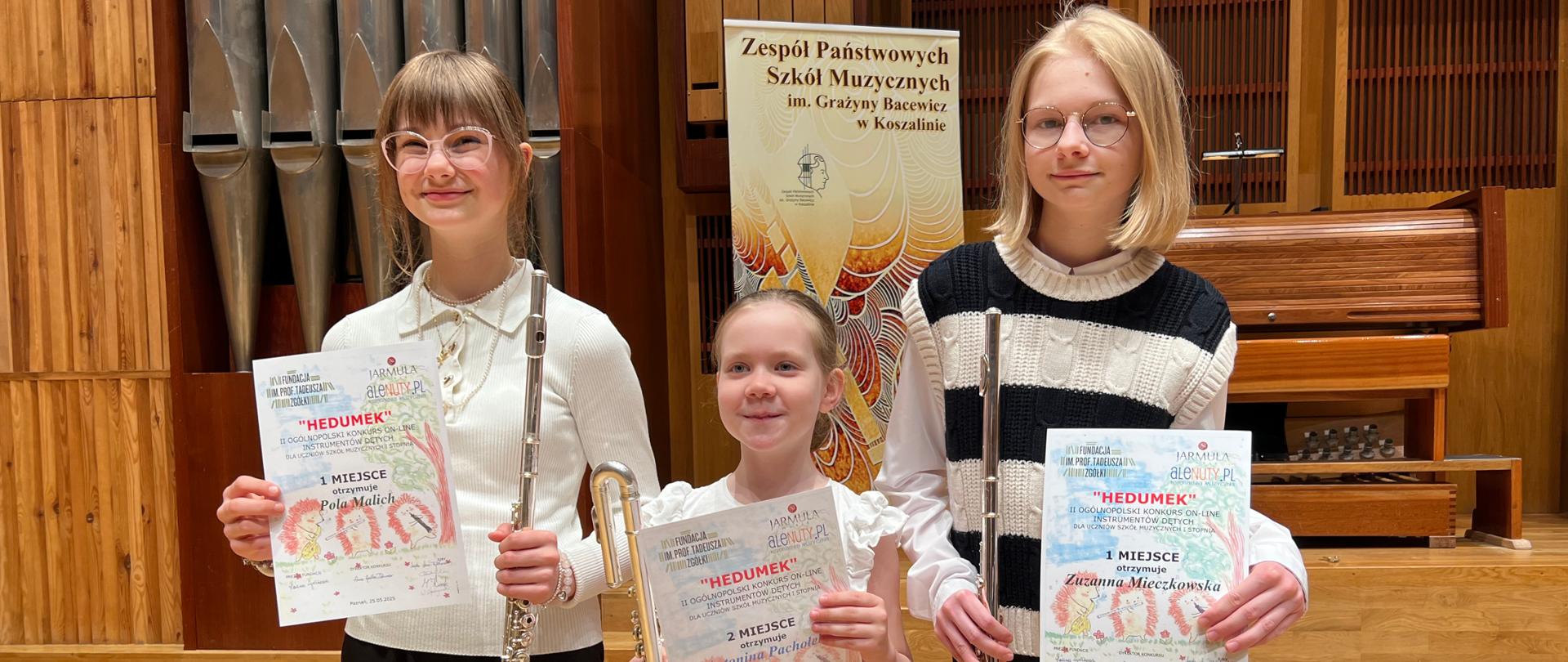Uczennice ZPSM trzymają w ręku flety poprzeczne i dyplomy, na tle organów w ZPSM