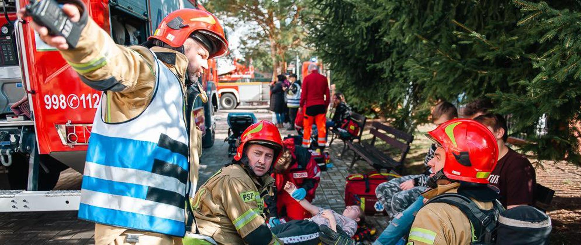 Strażacy udzielają pomocy medycznej poszkodowanym dzieciom w tle samochody gaśnicze