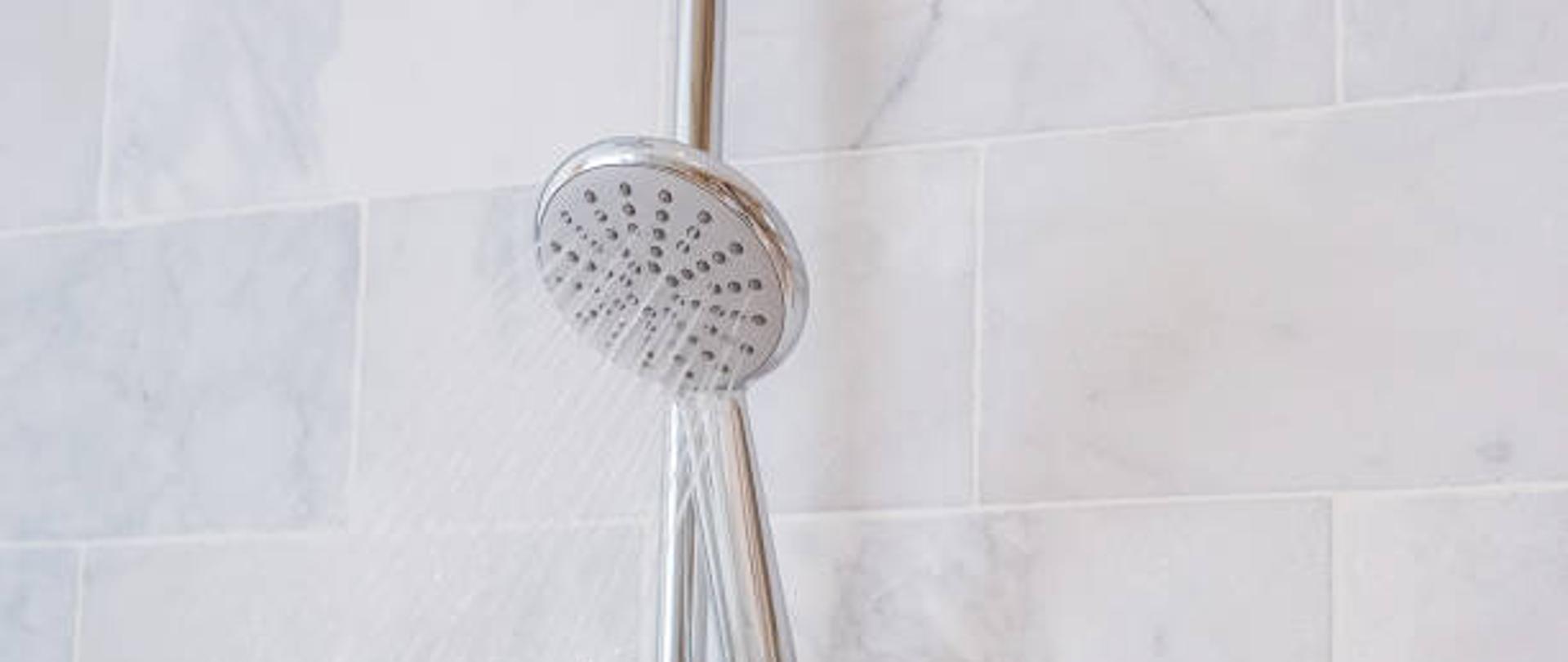 Krople wody rozpryskujące się lub płynące ze słuchawki prysznicowej i kranu na tle marmurowej ściany w nowoczesnej łazience